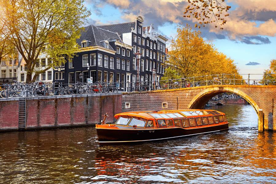 Canais de Amsterdão durante o outono com árvores em tons avermelhados.