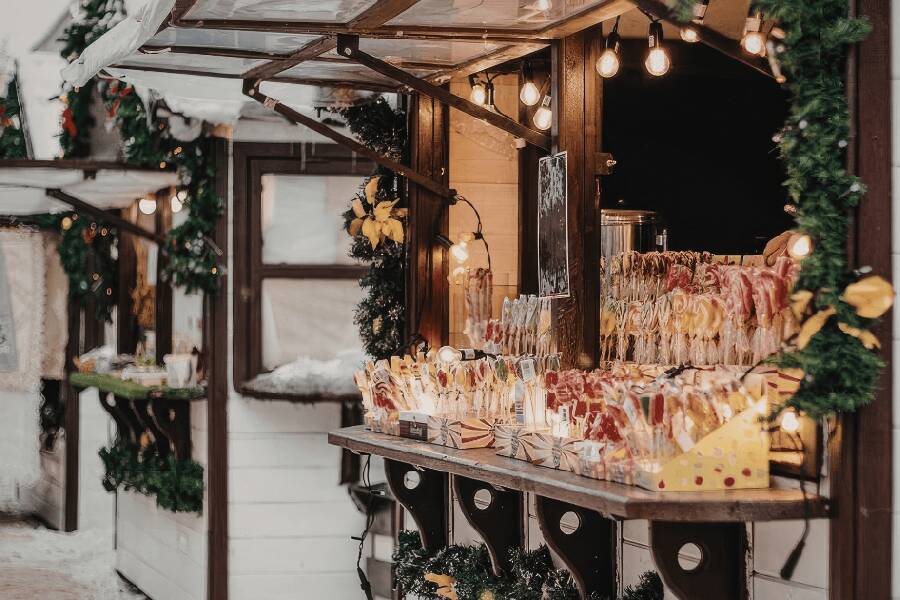 Banca de madeira num mercado de Natal com doces artesanais e luzes de decoração quentes.