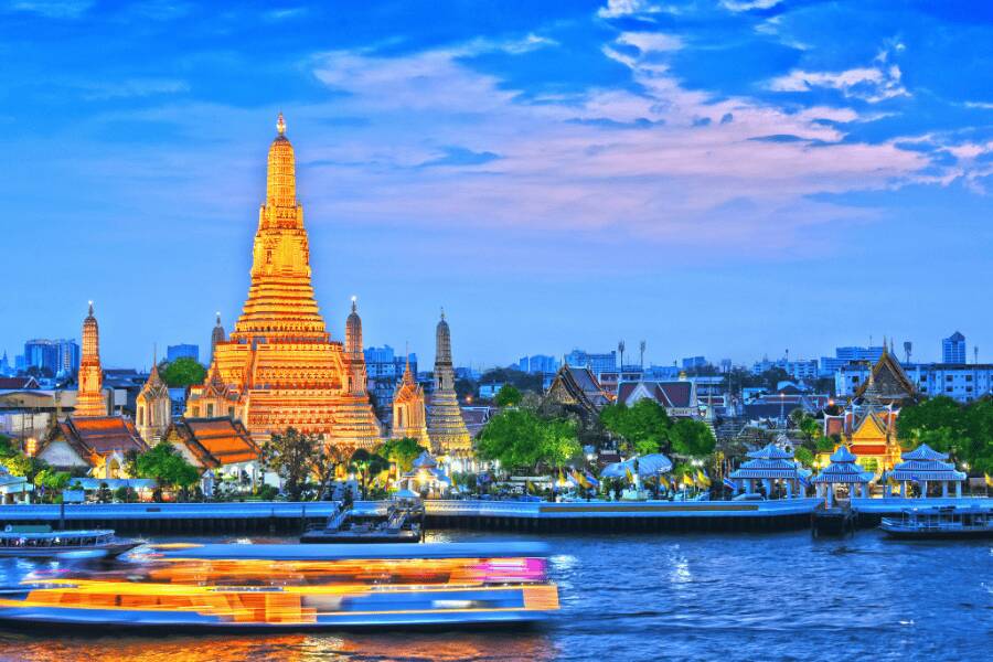 Templo Wat Arun iluminado ao anoitecer junto ao rio Chao Phraya em Banguecoque