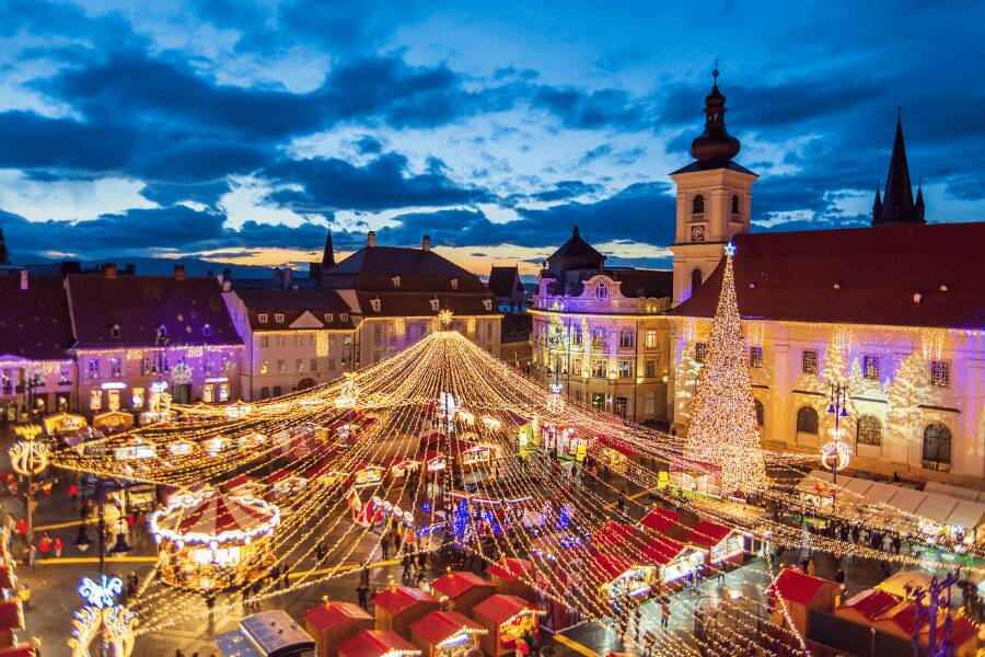 Vista aérea do mercado de Natal na praça principal de Sibiu com luzes natalícias e grande árvore iluminada.
